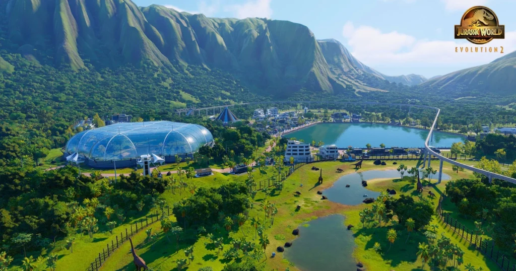 A video game screenshot of Jurassic World Evolution 2. The image shows a lush, tropical island with a large research facility, a monorail track, and several dinosaur enclosures. Different species of dinosaurs, including Brachiosaurus and Tyrannosaurus Rex, can be seen roaming their habitats.