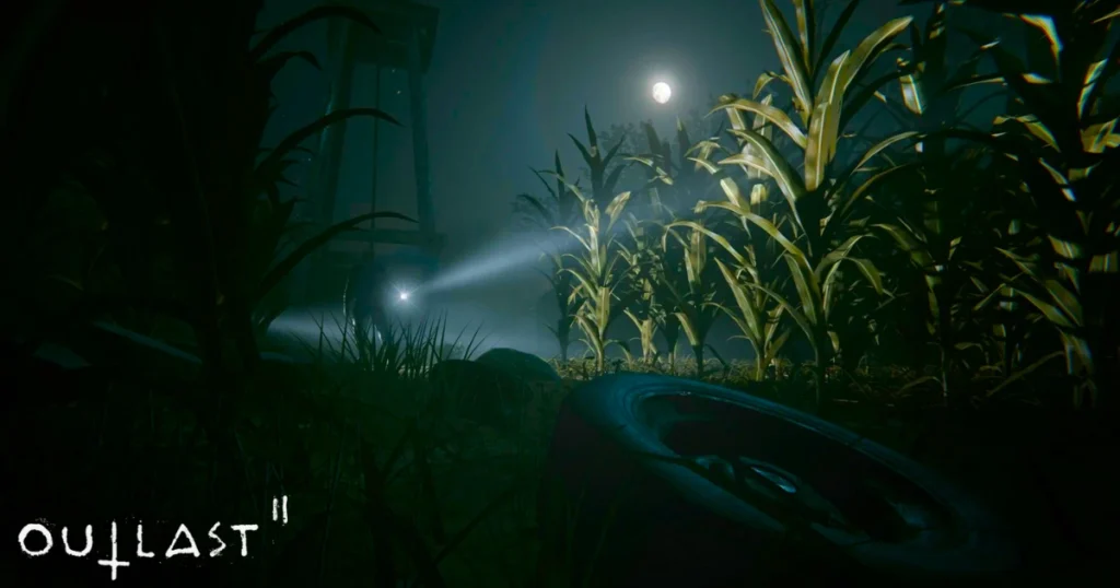 A dark, eerie scene from Outlast 2. The player character's flashlight illuminates a cornfield at night, casting long shadows and creating a sense of dread. The moon shines brightly overhead, adding to the unsettling atmosphere. A discarded tire lies in the foreground, hinting at the potential dangers lurking within the field.